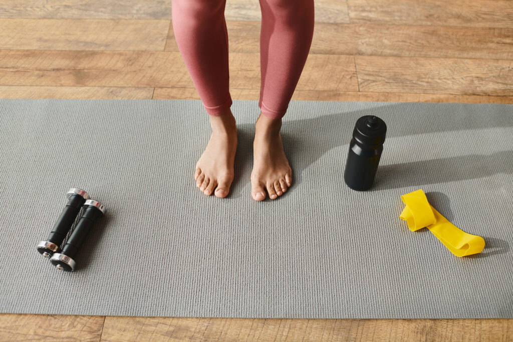 Frau in Sportbekleidung, die auf einer Yogamatte steht, neben ihr ein Paar Füße.